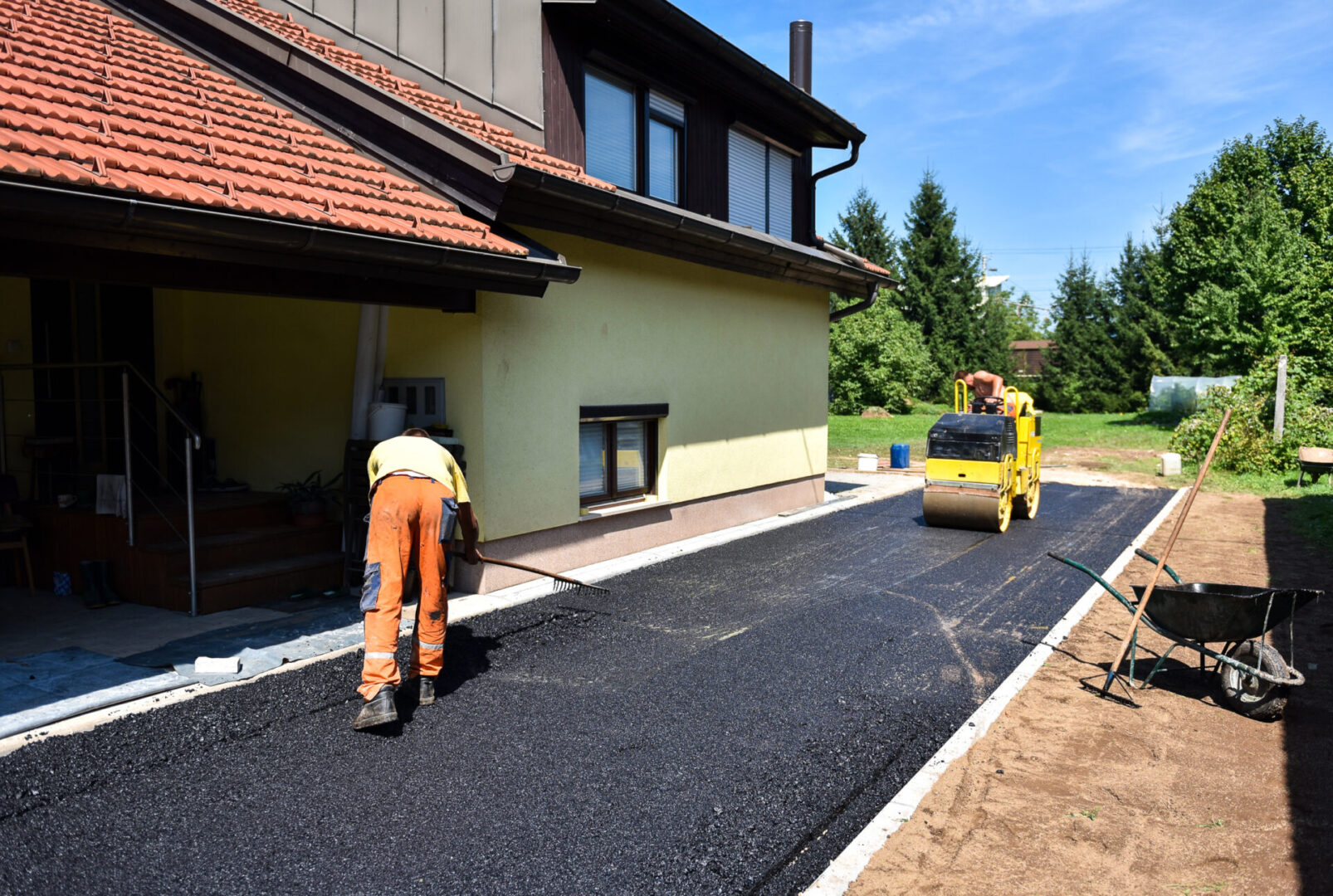 Team of Workers making and constructing asphalt road construction with steamroller. The top layer of asphalt road on a private residence house driveway