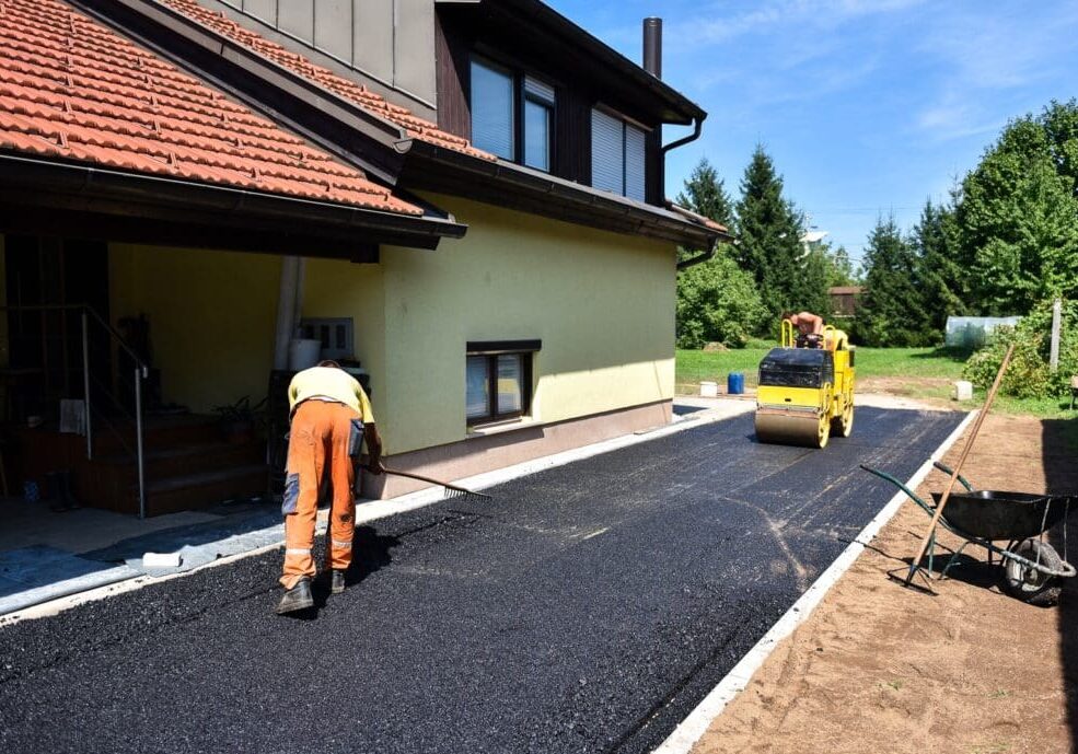 Team of Workers making and constructing asphalt road construction with steamroller. The top layer of asphalt road on a private residence house driveway